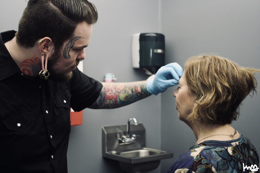 A person with tattoos on their face getting his ear cleaned.